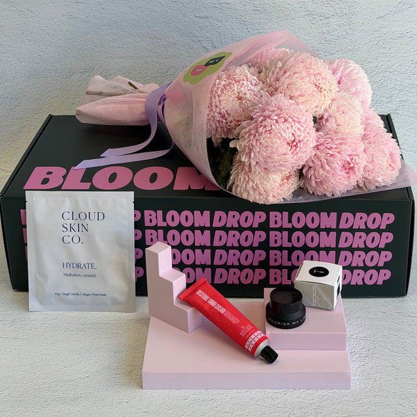 Bloom Drop product set with pink flowers, skincare items, and a box on a light gray background.