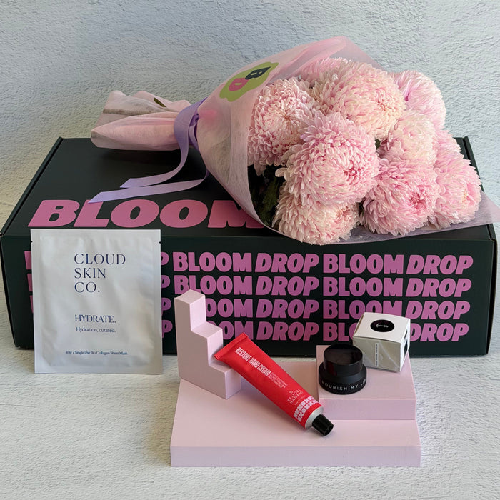 Bloom Drop product set with pink flowers, skincare items, and a box on a light gray background.