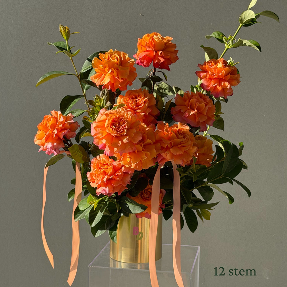 12 orange Colombian roses hand-reflexed with foliage in a brushed gold rose pot by Bloom Drop Sydney