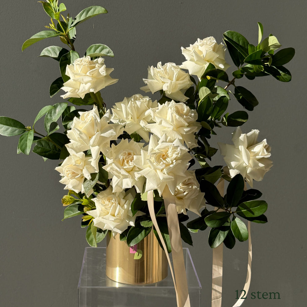 12 white Colombian roses hand-reflexed with foliage in a brushed gold rose pot by Bloom Drop Sydney