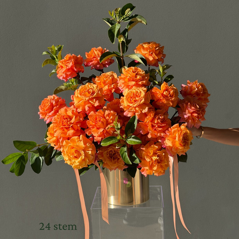 24 orange Colombian roses hand-reflexed with foliage in a brushed gold rose pot by Bloom Drop Sydney