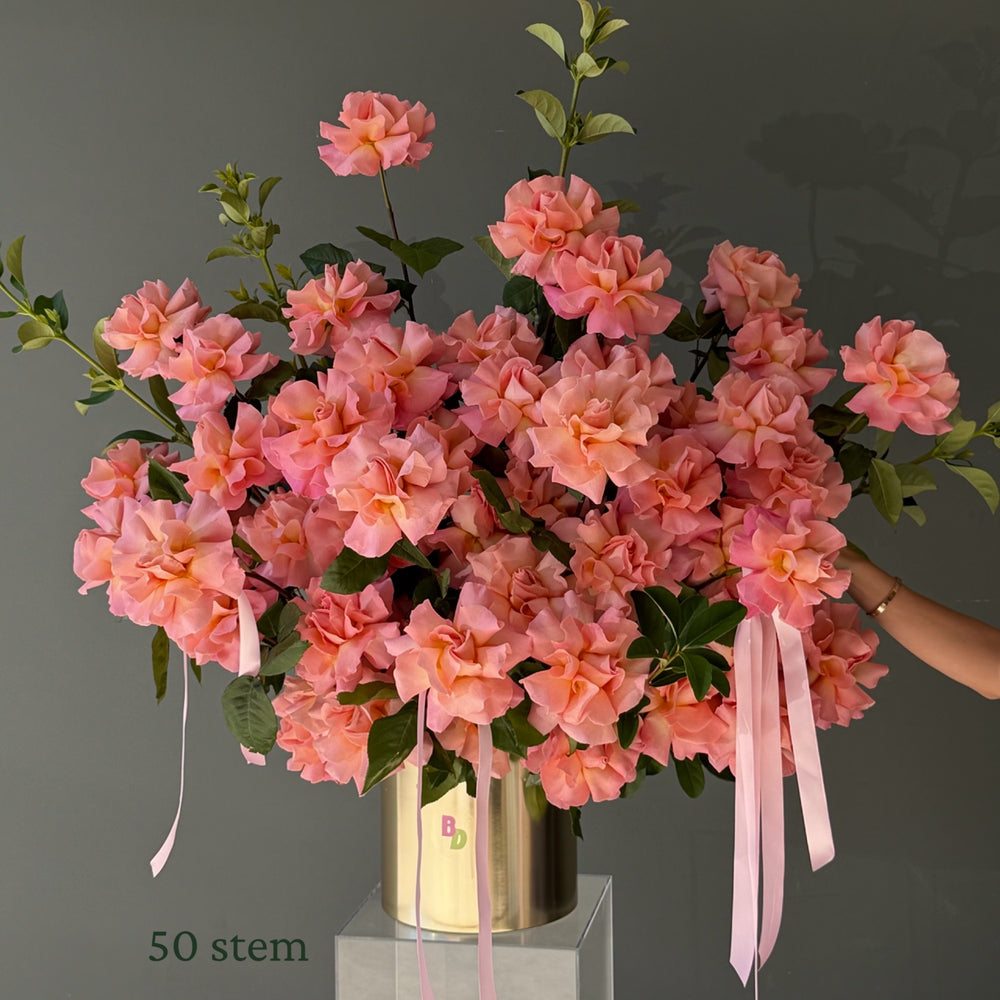 50 peachy pink Colombian roses hand-reflexed with foliage in a luxury brushed gold rose pot by Bloom Drop Sydney