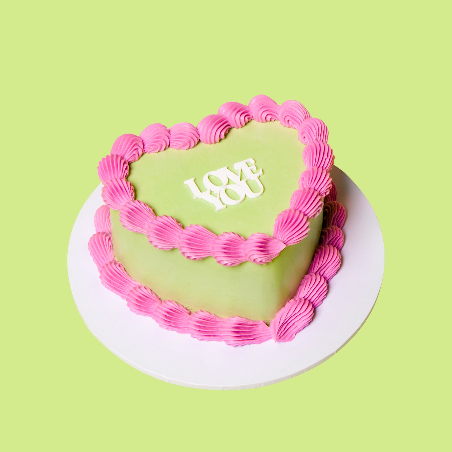 Heart-shaped cake with pink frosting and 'LOVE' written on a green background