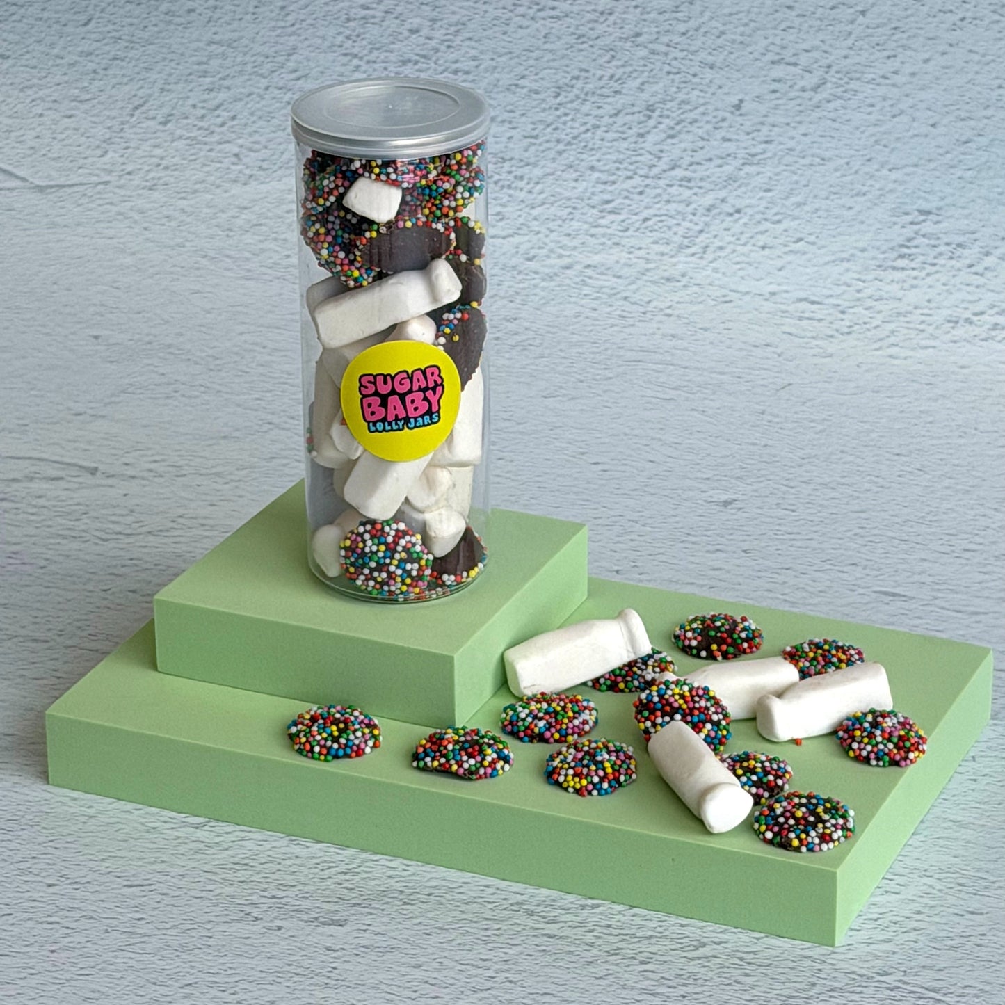 Jar of chocolate-covered treats with sprinkles on a green platform against a light blue background