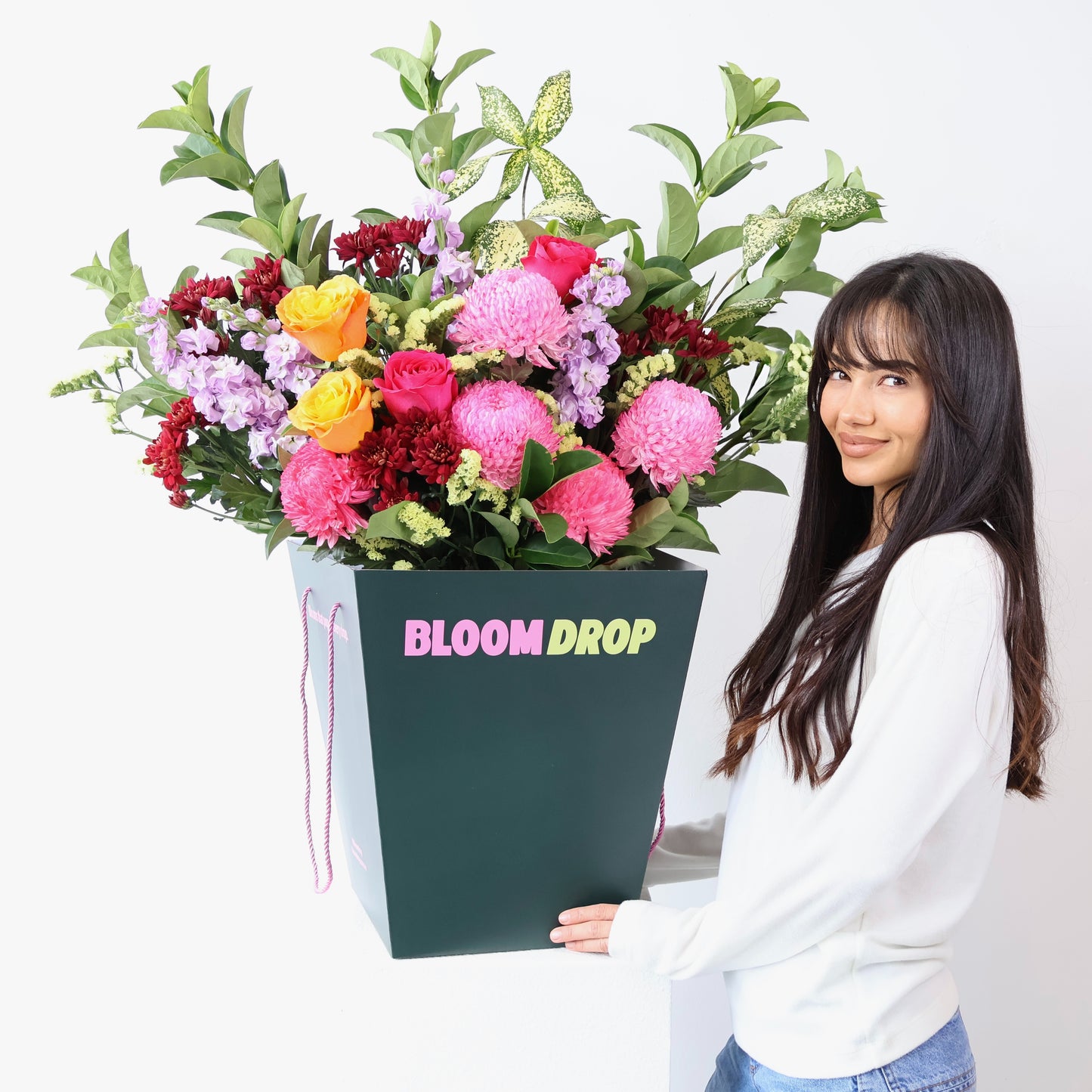 Woman holding a large bouquet of flowers in a box labeled 'Bloom Drop' against a white background