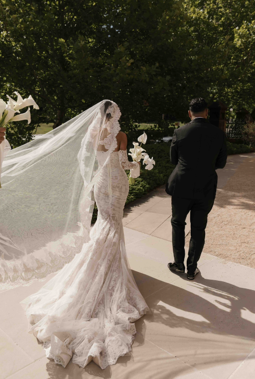 Woman in a wedding dress with a long veil walking outdoors.
